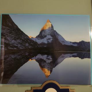 A serene view of a majestic mountain reflecting in a calm lake during sunrise.