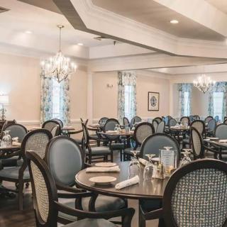 An elegant dining room with neatly arranged tables and chairs, illuminated by chandeliers.