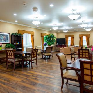 A well-lit dining area with wooden floors, tables, and chairs arranged neatly throughout the room.