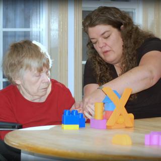 A caregiver assists an elderly person in playing with colorful blocks.