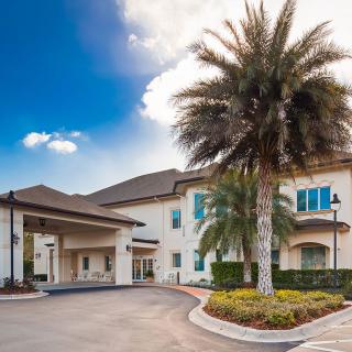 A modern building with a palm tree and driveway under a blue sky with clouds.