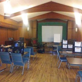 A spacious meeting room with chairs and tables set up for a session, featuring a whiteboard at the front.