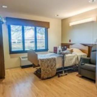 A well-lit hospital room with a bed, chair, and large window.
