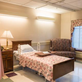 A cozy hospital patient room featuring a bed, a comfortable chair, and warm lighting.