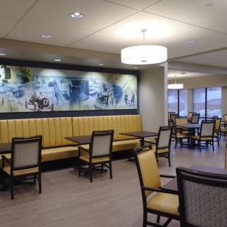 A modern dining area with yellow upholstered seating, wooden chairs, and decorative artwork on the wall.