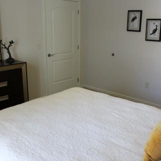 A minimalist bedroom with a simple bed, two bird-themed wall pictures, and a small dresser.