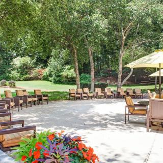 A beautiful outdoor patio area with chairs, tables, and umbrellas surrounded by lush greenery and colorful flowers.