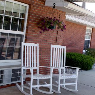Two white rocking chairs on a porch with a hanging plant.