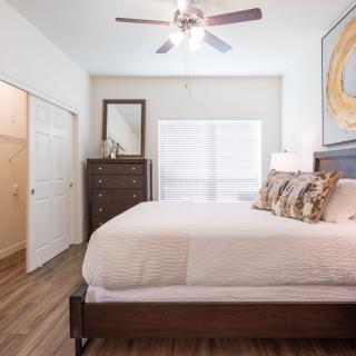A modern bedroom with a neatly made bed, a dresser with a mirror, and a ceiling fan.