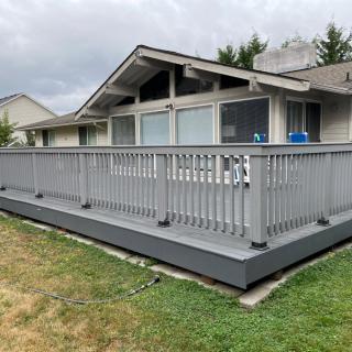 A wooden deck attached to the back of a house, featuring railings and overlooking a grassy backyard.