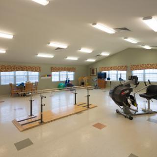 A spacious physical therapy gym equipped with various exercise machines and parallel bars for rehabilitation.