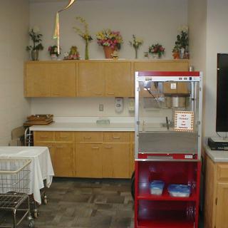 A kitchenette area featuring a popcorn machine, countertop with overhead cabinets, and decorative flowers.
