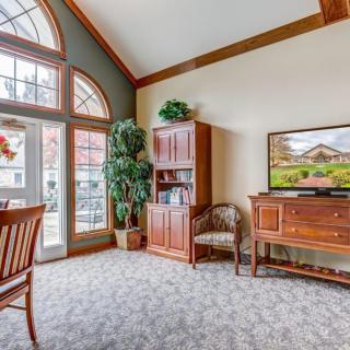 A cozy living room interior with wooden furniture, large windows, and a television.