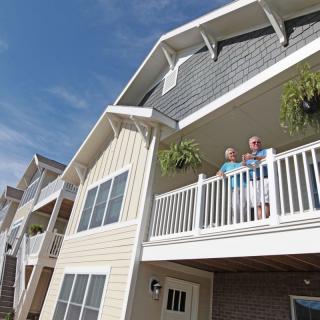 Two people standing on a residential balcony of a multi-story building.