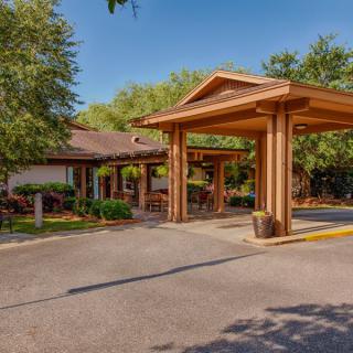 A building entrance with a covered driveway surrounded by trees under a clear blue sky.