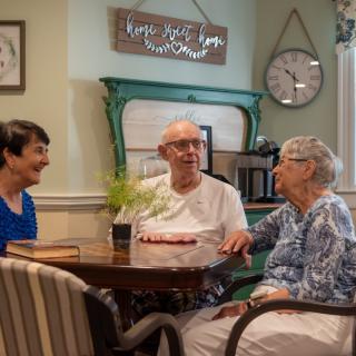 A group of three people sitting at a table, engaged in a friendly conversation in a cozy living room setting.