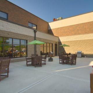 A spacious outdoor patio area with tables, chairs, and umbrellas next to a brick building under a clear blue sky.