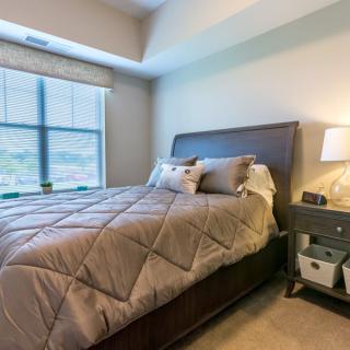 A cozy bedroom with a large bed, nightstand, and window offering natural light.