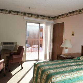 A tidy hotel room with a bed, desk, and sliding glass door letting in natural light.
