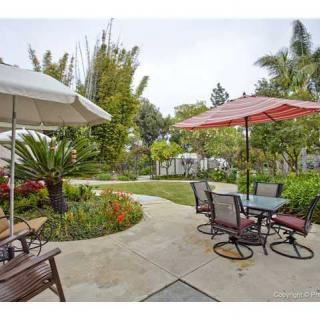 A well-maintained garden patio with furniture and umbrellas, surrounded by lush greenery.