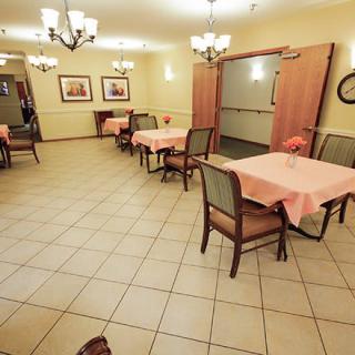 A spacious dining area with several tables and chairs, decorated with chandeliers and lit warmly, featuring a tiled floor.