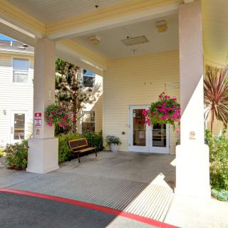 A covered building entrance with hanging plants and landscaping.