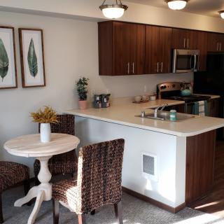 A modern kitchen with wooden cabinets, a small dining table, and stainless steel appliances.