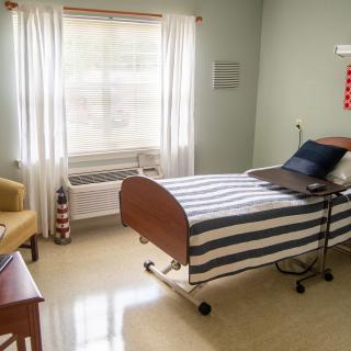 A clean and simple hospital room with a single bed and a window letting in natural light.