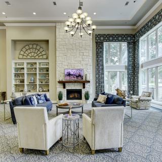 A luxurious living room with a chandelier, fireplace, and comfortable seating surrounded by large windows.