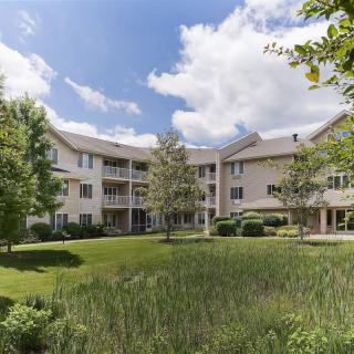 A residential apartment building surrounded by lush greenery and a well-maintained lawn under a partly cloudy sky.