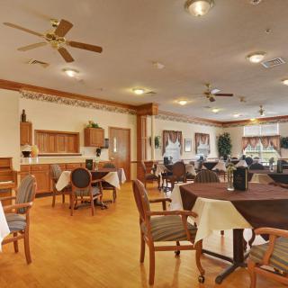 A spacious dining area with neatly arranged tables and chairs, featuring ceiling fans and wooden flooring.