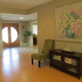 A cozy living room featuring a chair, a decorative table with books, and a large painting of flowers on the wall.