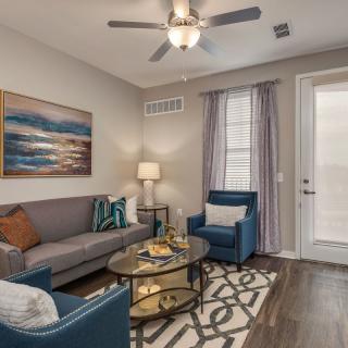 A cozy living room with modern furnishings, including a gray sofa, blue armchairs, and a glass coffee table on a patterned rug.