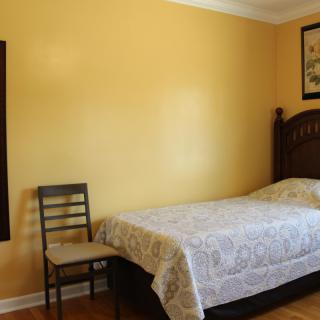 A minimalist bedroom with a single bed, chair, and yellow walls.