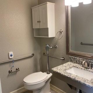 A small bathroom with accessible features including grab bars and a wall-mounted cabinet.