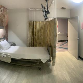 A hospital room with a single bed, television, and privacy curtain.