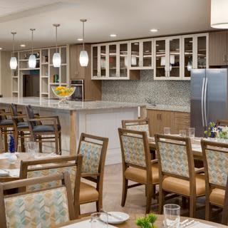 A modern kitchen and dining area featuring a bar counter with pendant lights, surrounded by wooden chairs and tables.