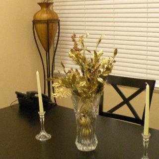 A dining table decorated with a vase of flowers and candles, with a lamp in the background.