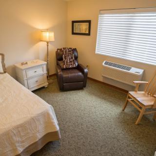 A cozy bedroom with a bed, armchair, and lamp by the window.