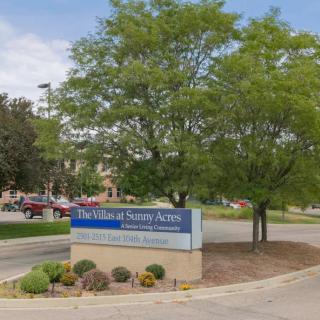 Entrance of a hospital with a sign, surrounded by trees and landscaping.