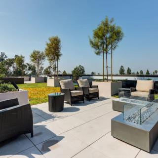 Modern outdoor patio area with comfortable seating and a fire pit surrounded by trees.