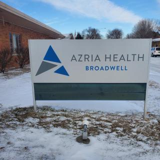 A sign for Azria Health Broadwell stands outside a building on a snowy day.