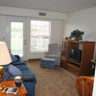 A cozy living room featuring a sofa, armchair, television on a wooden stand, and a large window.