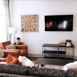A modern living room with stylish decor, featuring a wall-mounted TV, comfortable seating, and contemporary wall art.