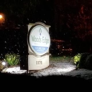 A illuminated sign for Woods Edge, visible in a snowy night setting.