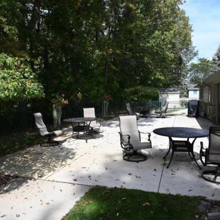 A peaceful backyard patio with chairs and tables under the shade of trees.