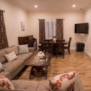 A cozy living room featuring a sofa, coffee table, dining area, and a piano with warm lighting.