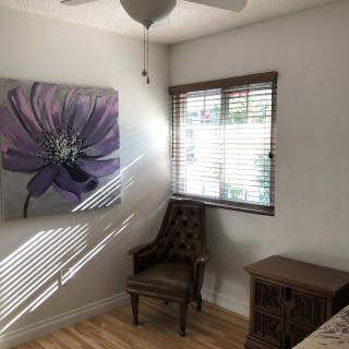 A cozy room with a large flower painting, a chair by the window, and wooden flooring.