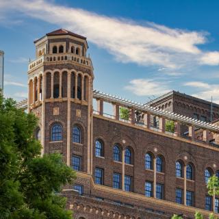 A historical brick building with a tower and arched windows surrounded by greenery.