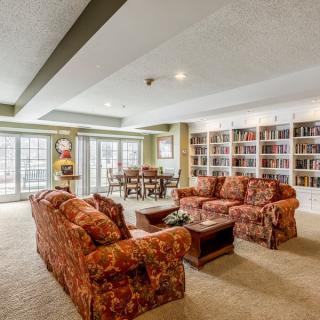 A spacious living room with patterned sofas, bookshelves, and large windows.